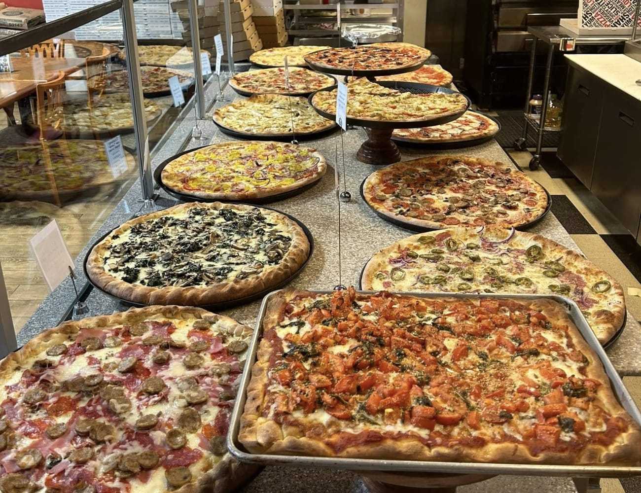 A variety of pizzas displayed on a counter, featuring different toppings and styles.